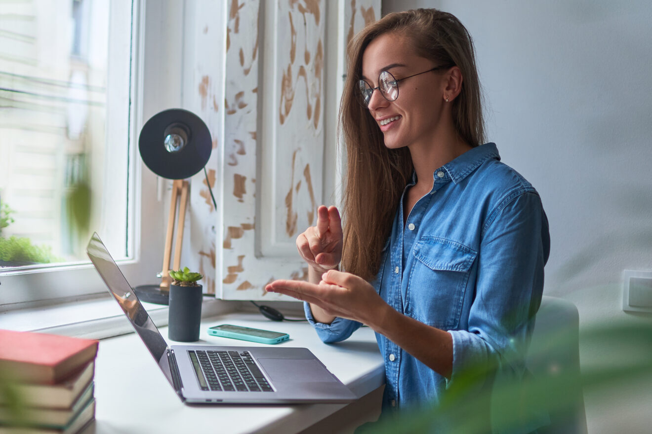 Junge Frau schaut auf einen Laptop und kommuniziert mit Gebärdensprache. 